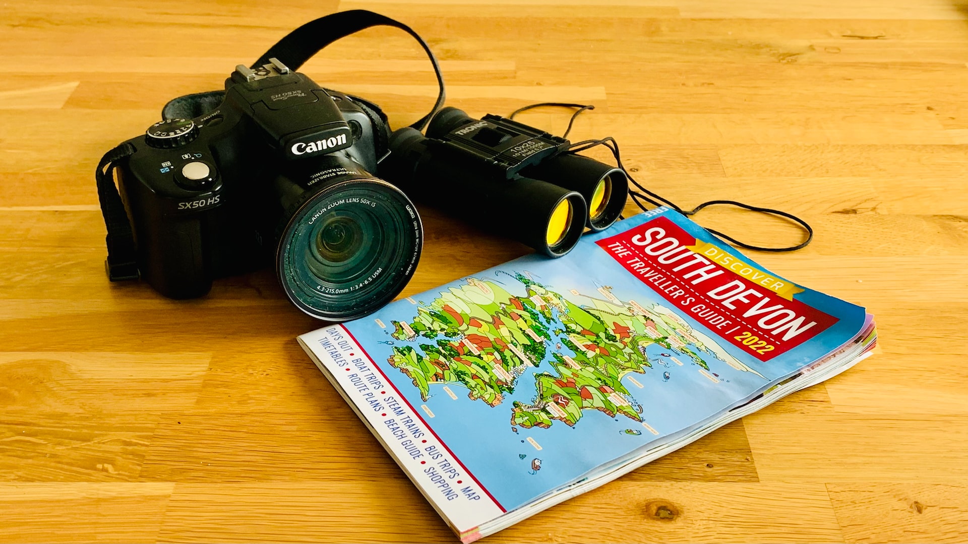 Camera, binoculars and a map on a wooden table