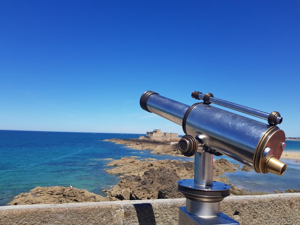 Image of telescope looking out over rocky bay with bright blue skies